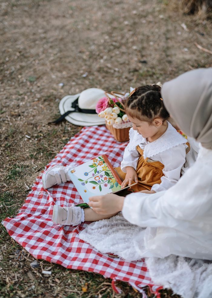 Heartwarming scene of a mother reading to her daughter on a picnic in a park.