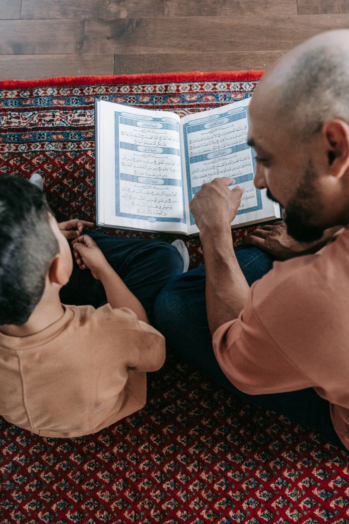 Father and son bonding over a book, sitting on a colorful carpet, focused on learning together.