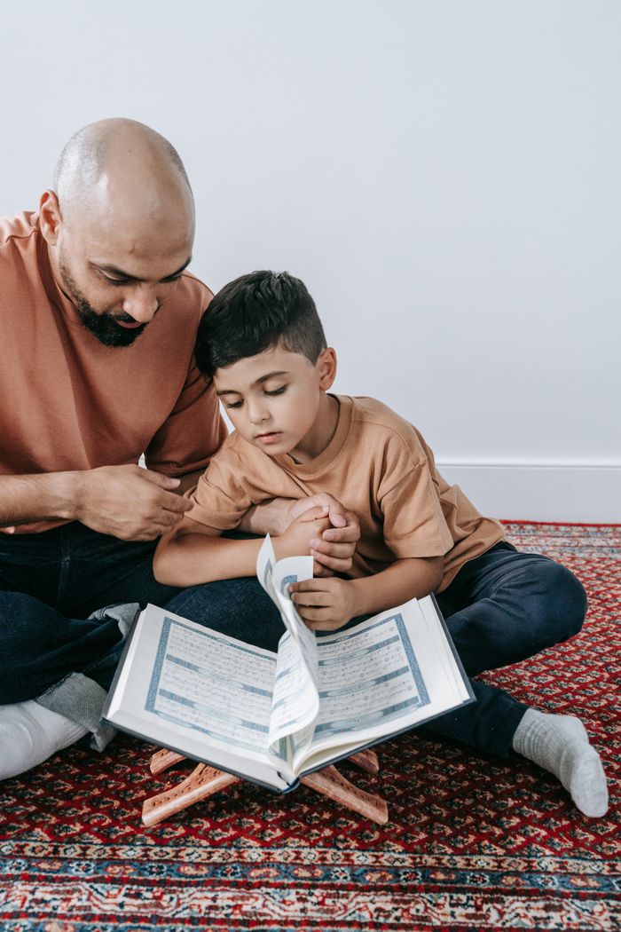 A father and son bonding over a book while sitting on a patterned carpet.